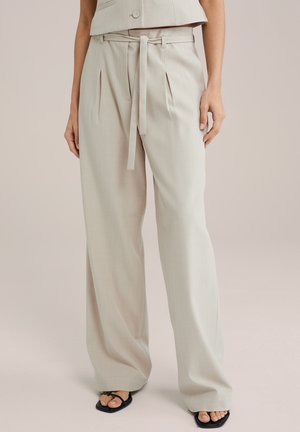 Hellegraue weit geschnittene Hose mit einem taillierten Bund, mit vorderen Falten und einer glatten Textur, kombiniert mit schwarzen Sandalen.
