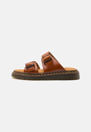 Brown leather slide sandals with two adjustable buckles, a cushioned insole, and a textured rubber sole, featuring a contrasting stitch detail.