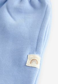 Tissu tricoté bleu clair avec un poignet froncé. L'étiquette présente un design simple de arc-en-ciel en tons terre sur un fond blanc.
