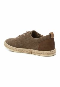 Zapatilla de lona marrón con media suela de yute trenzado, que presenta acentos de piel en el talón y cordones redondos. Punta redondeada y diseño de perfil bajo.