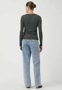 Koszula o dopasowanym kroju z długim rękawem, uszyta z ciemnoszarego materiału, zestawiona z jasnoniebieskimi, prostymi dżinsami. Oba elementy mają minimalistyczne detale szwów.