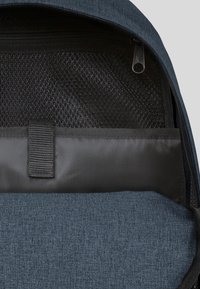 Tumma sininen reppu, jossa on teksturoitu kangas. Sisäpuolella on verkkotasku, sileä musta lokero ja keskikappale järjestämistä varten.
