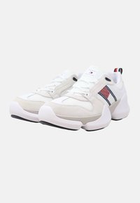 Scarpe da ginnastica bianche realizzate con un mix di rete e scamosciato. Presentano strisce rosse e blu navy, punta arrotondata, suola bianca spessa e logo sulla linguetta.