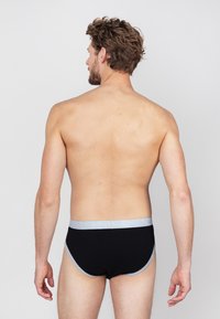 Zwarte boxershorts met een lichtgrijze tailleband, met een gladde textuur en een aansluitend ontwerp. Weergegeven op een blote torso vanuit een achteraanzicht.