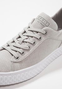 Jasnoszare płótna sneakersy z teksturowanego materiału, okrągły nos, szare metalowe oczka, sznurowadła i biała gumowa podeszwa z geometrycznym wzorem.