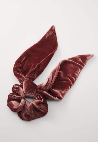 Südamikust valmistatud sametist juuksesideme, mis on tumepunase värviga ja millel on kaks pikka, teravat rippa. Kangas on pehme tekstuuriga ja kerge läikega, mis tõstab selle elegantsi.