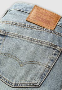 Jasnoniebieska tylna kieszeń dżinsów z denimu z pomarańczowym przeszyciem i beżową skórzaną metką Levi Strauss & Co., pokazująca rozmiar W32 L32 oraz numer serii 501.