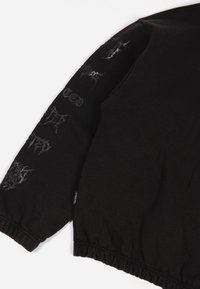 Felpa nera con vita e polsini elastici. Presenta del testo grafico argento sulla manica. Tessuto morbido e testurizzato. Design casual.