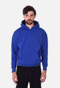 Felpa blu in cotone con tasca frontale, cappuccio con cordino e maniche a costine. Il tessuto appare morbido, con una vestibilità comoda.