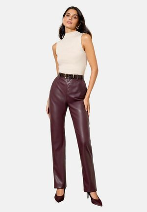 Burgunderfarbene Kunstlederhosen mit passgenauer Form, hoher Taille und vorderen Nahtdetails, kombiniert mit einem ärmellosen cremefarbenen Oberteil und einem schwarzen Gürtel.