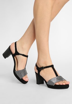 Black suede heeled sandals with a silver glitter strap and a T-bar design. Features a block heel and adjustable ankle strap.