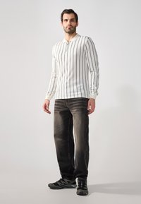 Chemise blanche à manches longues avec des rayures verticales bleu marine, associée à un jean foncé et des chaussures de sport noires avec des accents gris.