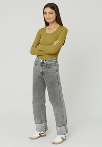 Haut à manches longues vert olive et jean en denim gris taille haute avec ourlets roulés. Baskets blanches avec des rayures noires. Design simple, style ajusté.