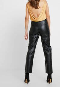 Black leather high-waisted pants with a straight cut, paired with a yellow draped back top, featuring spaghetti straps.