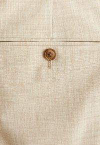 Beige Leinenstoff mit einem subtilen Texturmuster, featuring einem braunen Knopf mit vier Löchern und einem kontrastierenden Fadenstich.