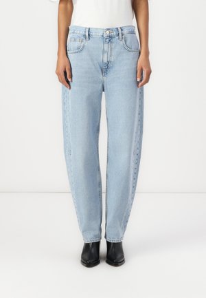 Jeans in denim blu chiaro con vestibilità ampia, vita alta, design a cinque tasche e dettagli in cucitura visibili, abbinati a stivali neri alla caviglia.