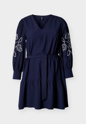 Tmavomodré šaty s výstrihom do V, nafúknutými rukávmi a vyšívanými kvetinovými detailmi na rukávoch. Majú opaskový pás a viacvrstvovú sukňu.