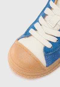 Baskets en daim bleu et cuir blanc avec embout en caoutchouc marron clair, lacets crème et coutures détaillées le long des bords. Semelle texturée.