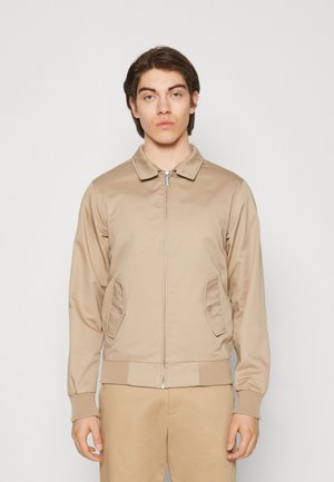 Veste bomber beige avec fermeture éclair à l'avant, col et poches latérales. Présente des poignets et un ourlet côtelés, une texture lisse et un design léger.