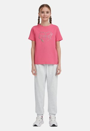 Lyserød bomulds t-shirt med korte ærmer, der har et glitrende hjertegrafik, parret med grå sweatpants og hvide sneakers.