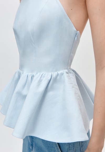 Haut péplum sans manches bleu clair avec fermeture éclair latérale, porté avec un jean bleu, vu de profil.