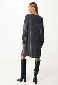 Graues Samtkleid mit langen Ärmeln, lockerer Passform, mittellanger Schnitt bis zur Oberschenkelmitte; kombiniert mit schwarzen knielangen Absatzstiefeln, glatte Textur.