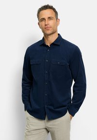 Marineblaue Hemdbluse mit langen Ärmeln, zwei Brusttaschen und einem Kragen. Der Stoff wirkt glatt und hat einen subtilen Glanz.