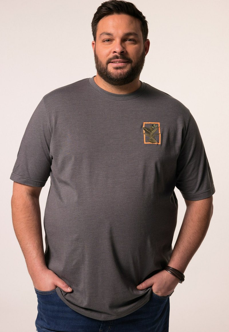 Šedé tričko s krátkým rukávem a kapsou, na kterém je zelený vzor rostliny orámovaný oranžovou barvou. Měkká textura a volný střih.