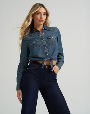 Jeansskjorte i mørkeblå farge med knapper, to brystlommer og knyttet nederkant. Myk tekstur med kontrasterende sømdetaljer. Vide benjeans i mørk farge.
