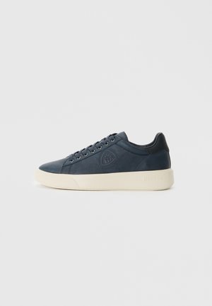 Dark blue sneaker with smooth leather, rounded toe, white rubber sole, and logo detailing on the side. Silver eyelets for laces.