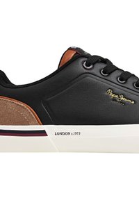 Zapatilla de cuero negra con detalles en gamuza marrón, suela blanca, cordones negros, logo dorado y la inscripción "LONDON s.1973" en el lateral.