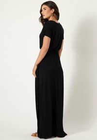 Czarna maxi sukienka z miękkiego materiału, z krótkimi rękawami, marszczoną talią i zwiewnym dołem. Gładka faktura i prosty design.