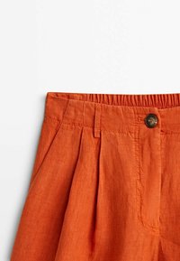 Pantalons en lin couleur terre cuite avec taille froncée, fermeture à bouton, passants de ceinture et plis à l'avant.