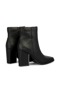 Botas de cuero negro hasta el tobillo con tachuelas plateadas, punta afilada y tacón cuadrado. Cierre de cremallera en la parte trasera, textura suave y color sólido.