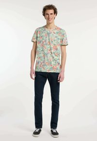 Korte mouw lichtgroen T-shirt met een bloemenpatroon in roze en blauw, gecombineerd met donkerblauwe spijkerbroek en zwarte sneakers.