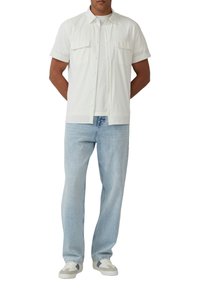 Korte mouwen witte overhemden met twee borstzakken, gecombineerd met lichtblauwe jeans en witte sneakers met grijze accenten.