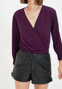Purple wrap top with long sleeves and elastic waistband, paired with black quilted leather shorts featuring a smooth texture and side pockets.