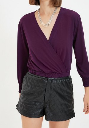 Paarse wikkeltop met lange mouwen en een elastische tailleband, gecombineerd met zwart, gequilted leren shorts met een gladde textuur en zijzakken.