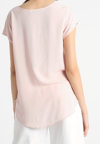 Ljusrosa, kortärmad topp med rundad halsringning, slät textur och en något böjd nederkant, designad för en avslappnad passform.