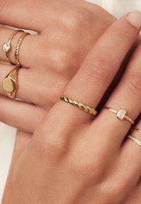 Goldringe in verschiedenen Designs: gedrehter Ring, glatter Ring, mit Steinen akzentuierter Ring und gravierte Stile, alle auf einer Hand mit natürlicher Hautstruktur präsentiert.