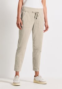 Pantalons jogger couleur beige clair avec une taille élastique et un cordon de serrage, dotés de deux poches avant et d'un design à jambes fuselées.