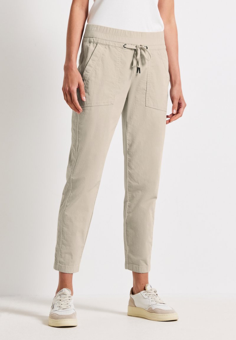 Pantalons jogger couleur beige clair avec une taille élastique et un cordon de serrage, dotés de deux poches avant et d'un design à jambes fuselées.