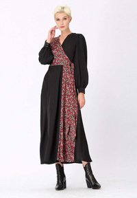 Robe noire avec des manches bouffantes et un détail floral en rouge et blanc. Le tissu est doux avec une silhouette fluide, associé à des bottes noires.