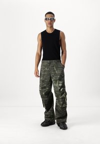 Svart ärmlös topp, kamouflage cargo byxor med flera fickor och svarta chunky sneakers. Modellen bär reflexglasögon.