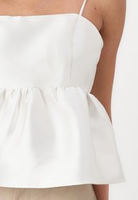 Hvit sateng peplum-top med tynne stropper, med en tettsittende overdelen og en samlet midje som skaper en svungne silhuett.