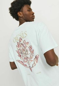 Lichtblauwe katoenen t-shirt met een grote, florale afbeelding in tinten van roze en rood op de achterkant, met daarboven de tekst "ORIGINALS".
