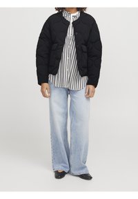 Černá prošívaná bunda s kulatým výstřihem a zapínáním na knoflíky, zkombinovaná s černobílým pruhovaným tričkem, širokými světle modrými džíny a černými botami.