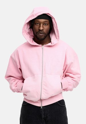 Pink zip-up hoodie with a large hood, front pockets, and ribbed hem cuffs. The fabric appears soft with a smooth texture.