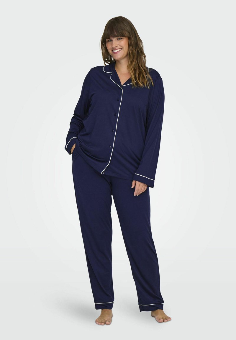 Marinblå pyjamasset med långa ärmar och byxor, med vit piping längs kragen och ärmslut, tillverkat av ett mjukt, slätt tyg.