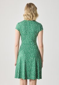 Green polka dot dress with short sleeves, fitted bodice, and flared skirt. Made of smooth fabric, featuring white circular patterns.